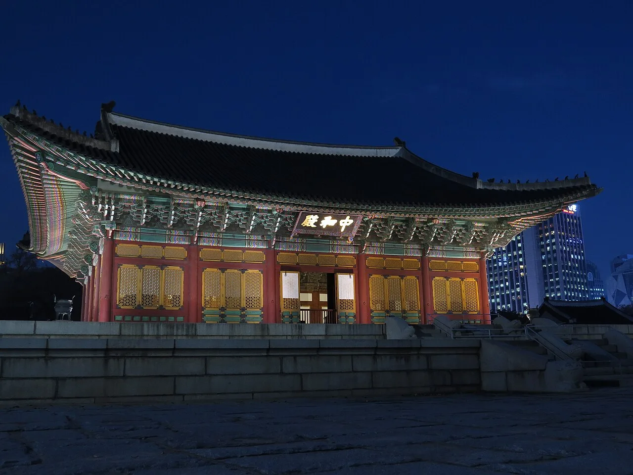 밤에 조명이 켜진 붉은 기둥의 덕수궁 중화전과 뒤쪽 고층 건물